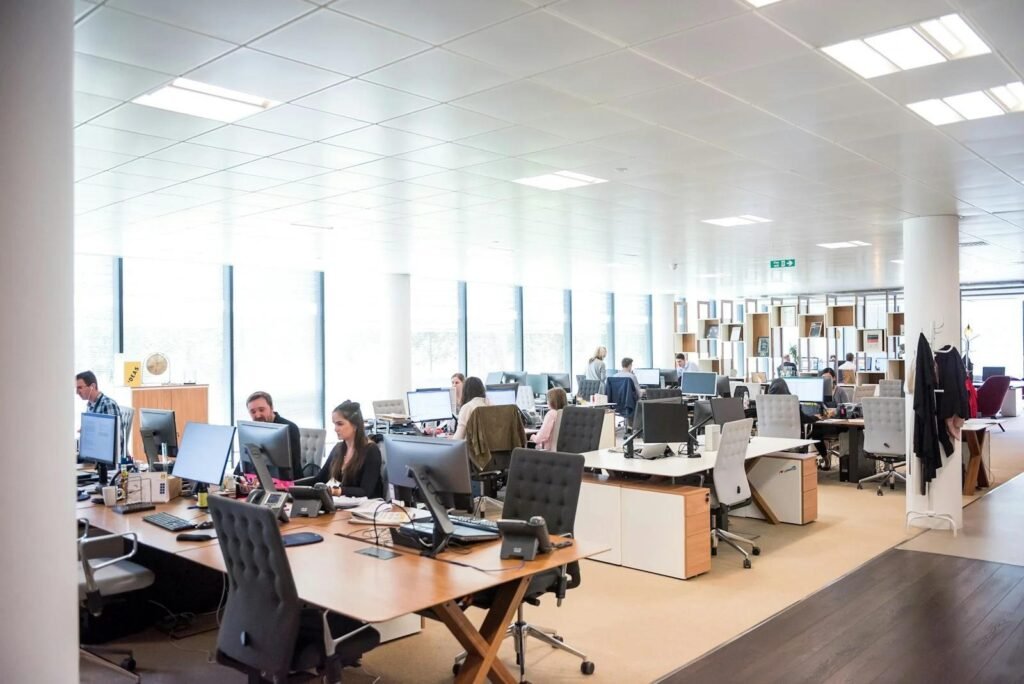 Bright and spacious office with employees working at desks, featuring large windows and a modern, open layout.