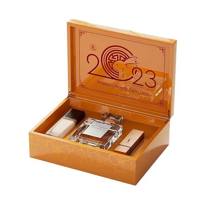 Open orange gift box with a "2023 Happy Chinese New Year" design, containing luxury perfume and cosmetics.