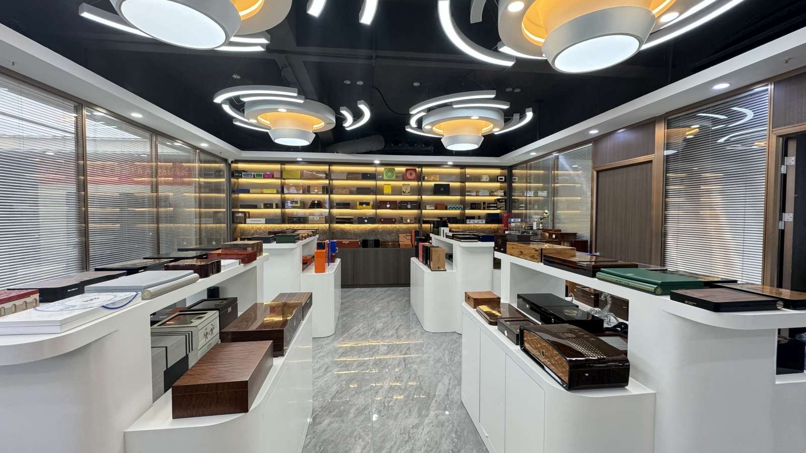 Modern showroom displaying a wide variety of luxury wooden boxes on sleek white counters with illuminated shelves in the background.