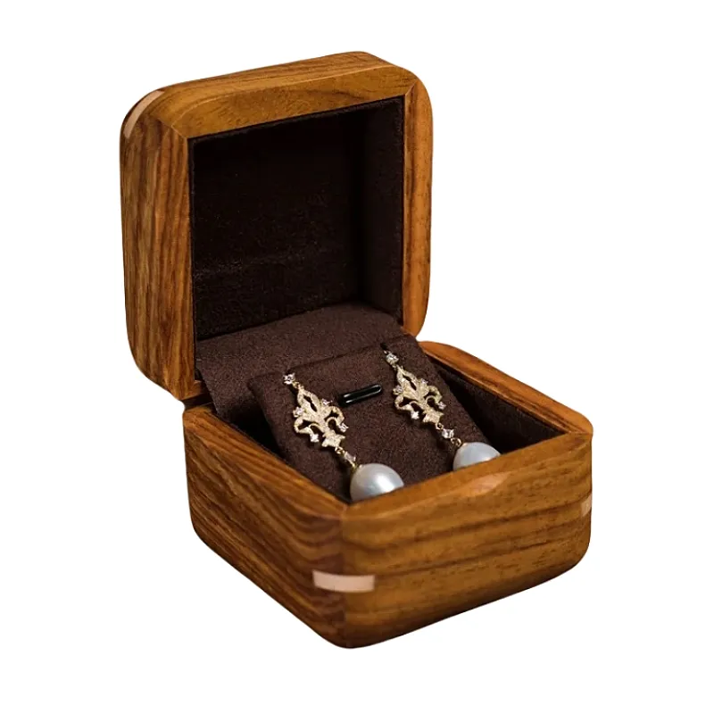 Compact wooden jewelry box with soft velvet lining, showcasing a pair of pearl and gold earrings.